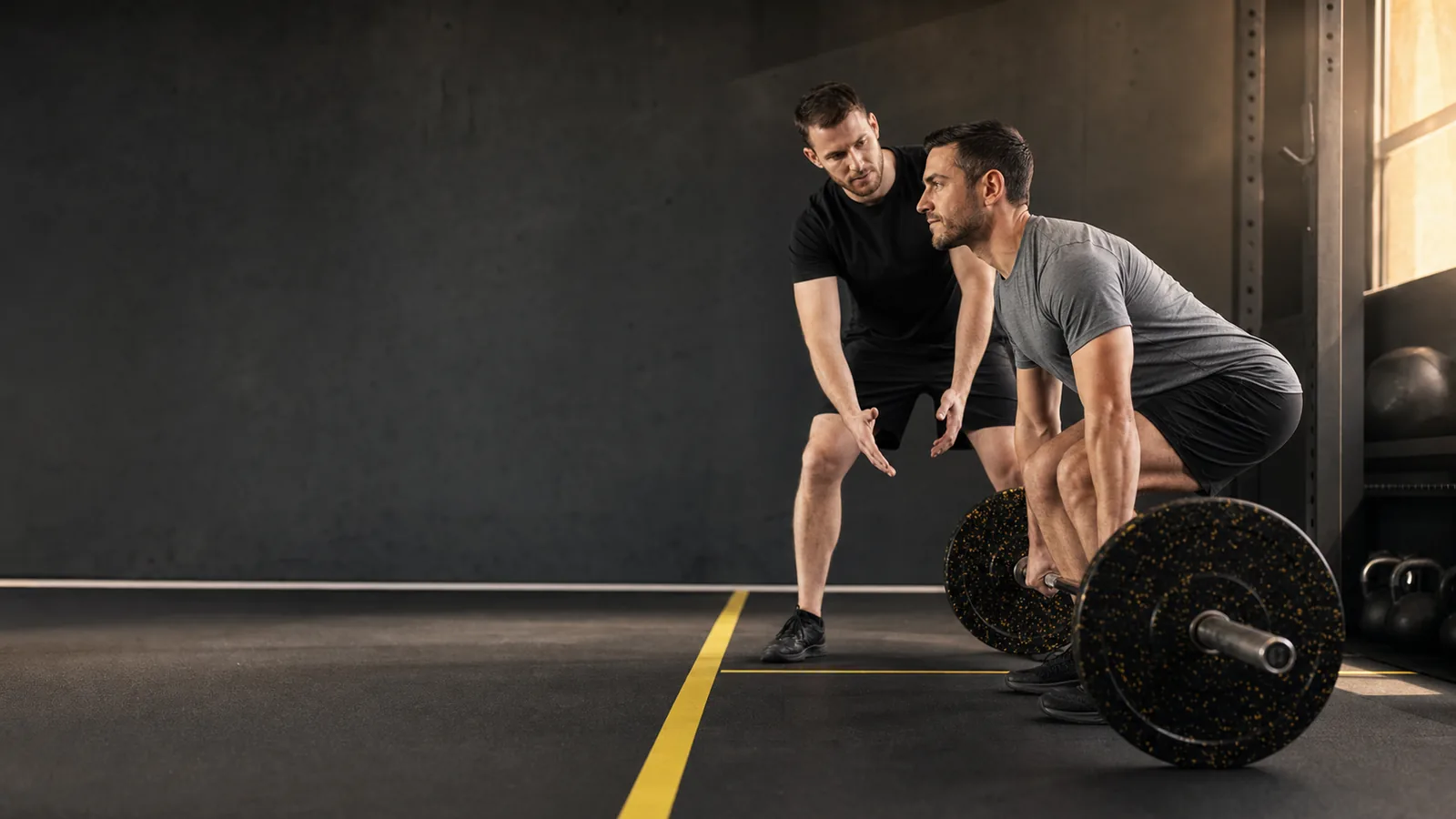 A personal trainer coaching a client through a deadlift in a training studio